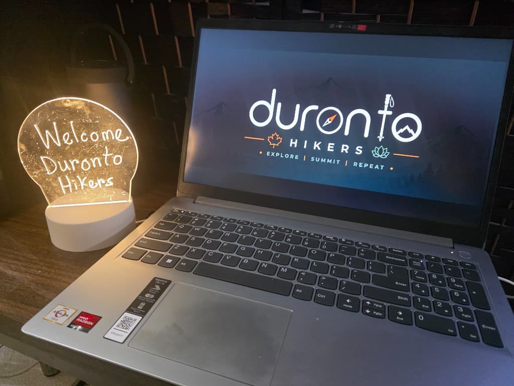 Laptop displaying the Duronto Hikers logo beside an illuminated Welcome Duronto Hikers sign