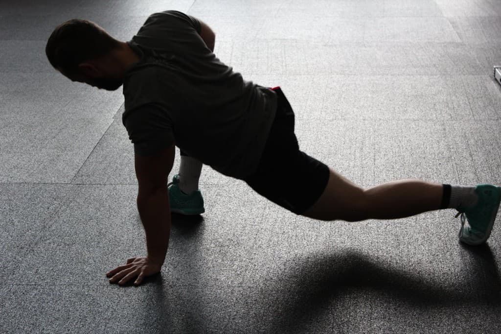 Man in athletic wear performing a deep lunge stretch on a gym floor under dramatic side lighting
