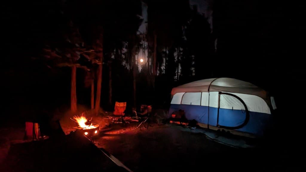 Camping tent and campfire at night in the forest under a full moon